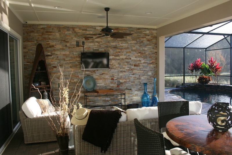 Norstone Aztec Stacked Stone Veneer used on an outdoor feature wall in a small screened in lanai with outdoor lounge furniture and an outdoor television